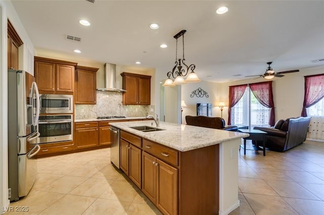 kitchen featuring visible vents, brown cabinetry, wall chimney exhaust hood, a sink, and appliances with stainless steel finishes