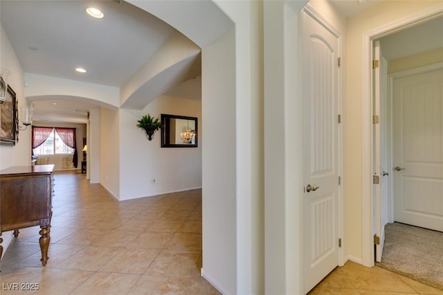 hall featuring baseboards, arched walkways, light tile patterned floors, and recessed lighting