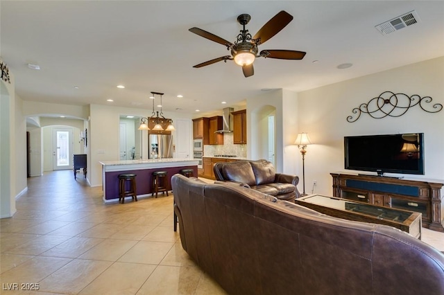 living room with a ceiling fan, visible vents, arched walkways, light tile patterned floors, and recessed lighting