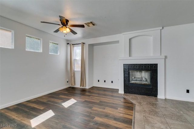 unfurnished living room featuring ceiling fan, visible vents, a fireplace, wood finished floors, and baseboards