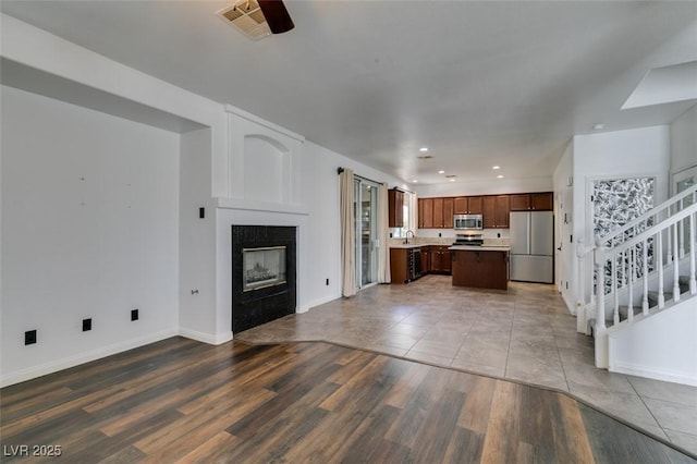 unfurnished living room with baseboards, a tiled fireplace, wood finished floors, and stairway