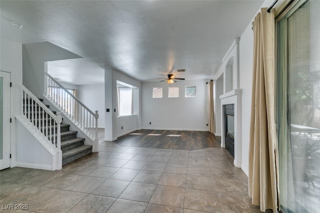 unfurnished living room featuring stairs, baseboards, tile patterned floors, a tile fireplace, and a ceiling fan