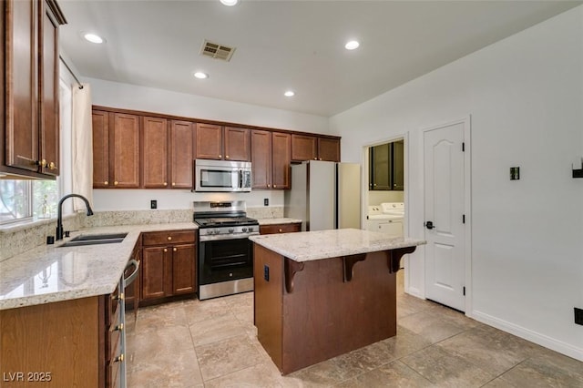 kitchen featuring appliances with stainless steel finishes, a sink, a breakfast bar area, a kitchen island, and washing machine and dryer