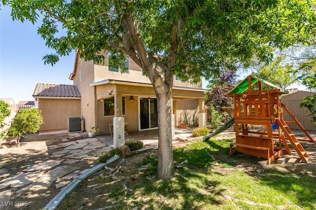 rear view of property with fence, stucco siding, a shed, a playground, and a patio