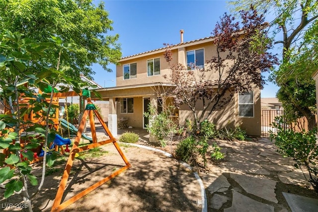 rear view of house featuring fence, a tile roof, stucco siding, a playground, and a patio