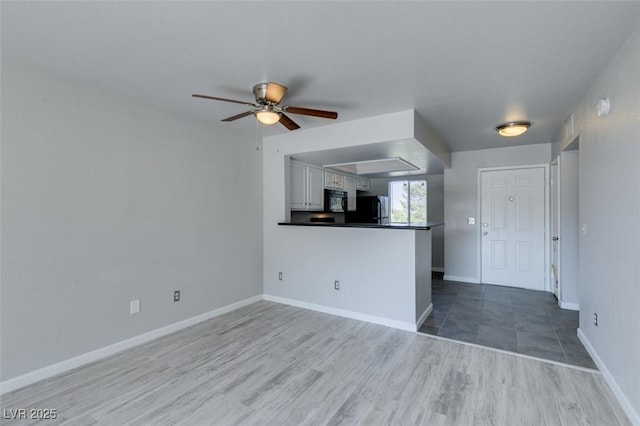 unfurnished living room with a ceiling fan, baseboards, and wood finished floors