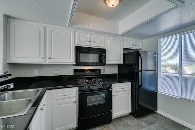kitchen featuring dark countertops, baseboards, white cabinetry, a sink, and black appliances