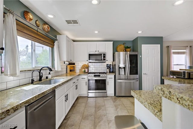 kitchen featuring decorative backsplash, visible vents, appliances with stainless steel finishes, a sink, and white cabinets
