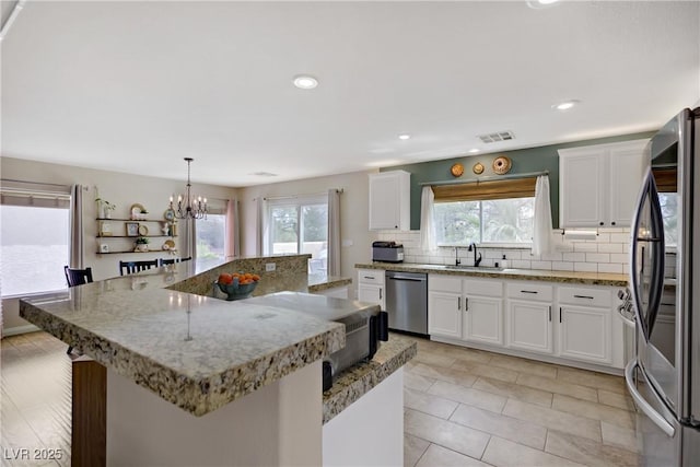 kitchen with decorative backsplash, white cabinetry, a chandelier, a sink, and appliances with stainless steel finishes
