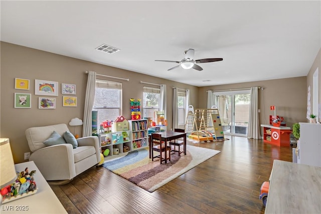 recreation room with plenty of natural light, a ceiling fan, dark wood finished floors, and visible vents