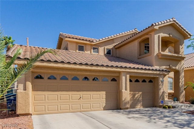 mediterranean / spanish house featuring an attached garage, a tiled roof, concrete driveway, and stucco siding