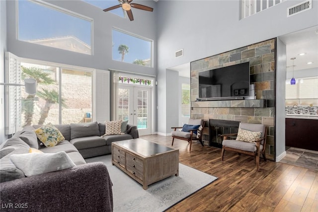living area with visible vents, a towering ceiling, ceiling fan, and hardwood / wood-style floors