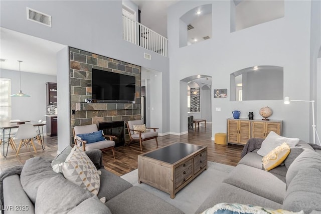 living room with arched walkways, baseboards, wood finished floors, and visible vents