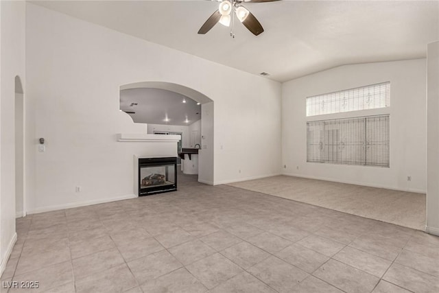 unfurnished living room featuring a multi sided fireplace, ceiling fan, arched walkways, vaulted ceiling, and light tile patterned flooring