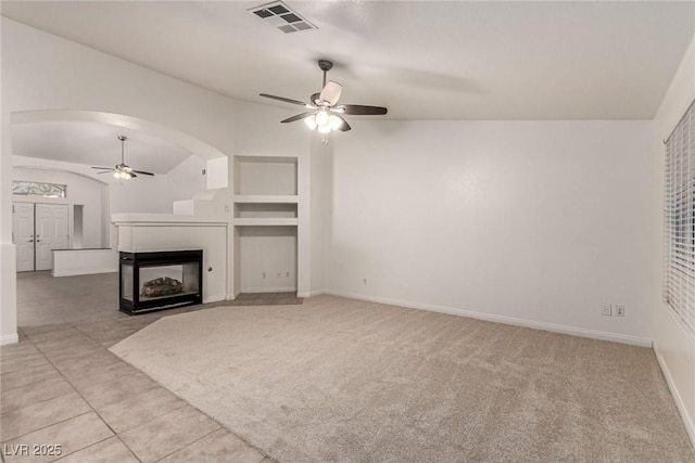 unfurnished living room featuring ceiling fan, visible vents, arched walkways, vaulted ceiling, and carpet floors