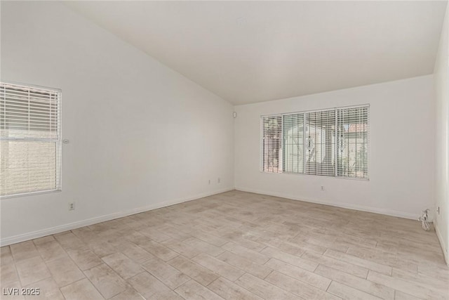 spare room with baseboards, light wood finished floors, and lofted ceiling