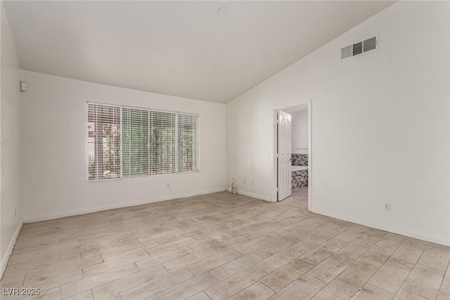 unfurnished room featuring baseboards, visible vents, light wood finished floors, and vaulted ceiling
