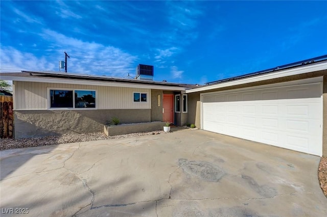 ranch-style home with an attached garage, concrete driveway, and solar panels