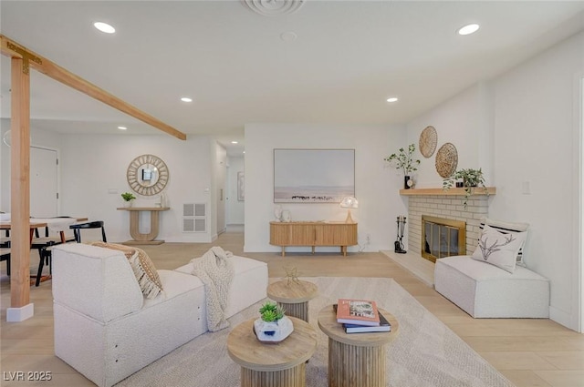 living area with light wood-style floors, a brick fireplace, recessed lighting, and visible vents