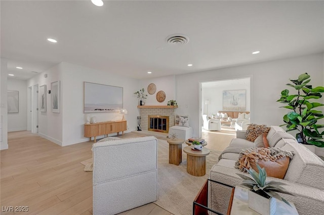 living room featuring recessed lighting, a brick fireplace, light wood-type flooring, and visible vents
