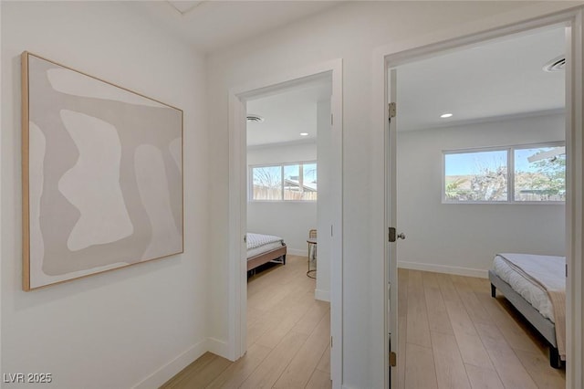 hallway featuring light wood-type flooring, baseboards, and a healthy amount of sunlight