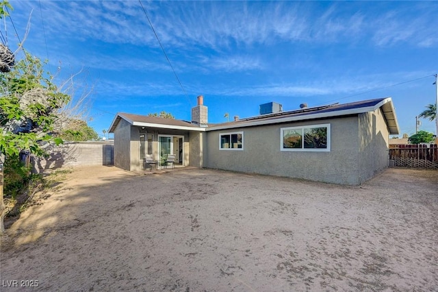 back of house with stucco siding, fence, and a chimney