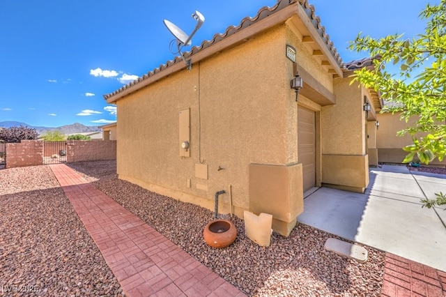 view of side of home with fence, a tile roof, stucco siding, a gate, and a mountain view