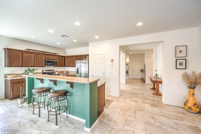kitchen featuring light stone countertops, appliances with stainless steel finishes, a breakfast bar area, recessed lighting, and visible vents