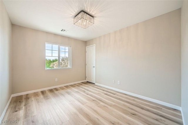 empty room with baseboards, light wood finished floors, a notable chandelier, and visible vents