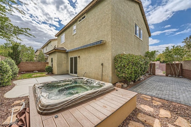 rear view of house with an outdoor hot tub, a fenced backyard, a patio area, and stucco siding