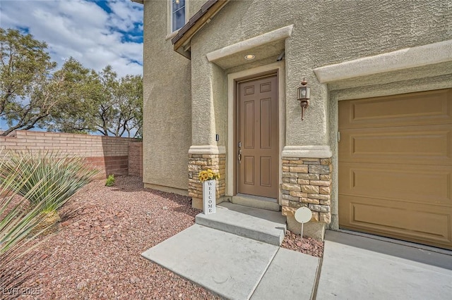 entrance to property featuring stucco siding, a garage, fence, and stone siding