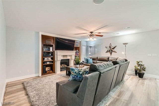 living room with baseboards, a ceiling fan, light wood-style flooring, and a fireplace