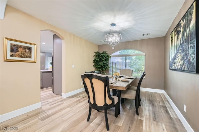 dining space featuring light wood-type flooring, arched walkways, baseboards, and visible vents