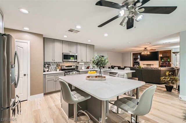 kitchen with gray cabinets, a ceiling fan, appliances with stainless steel finishes, light countertops, and light wood-style floors