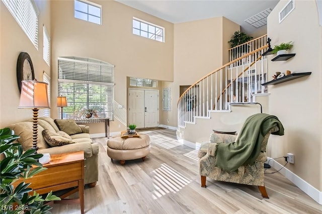living area featuring stairway, a towering ceiling, wood finished floors, and visible vents