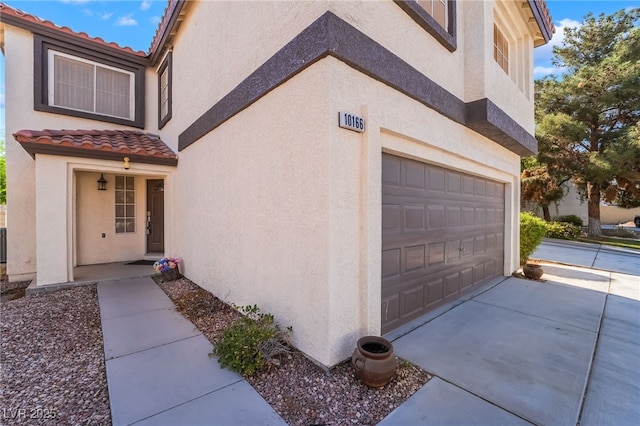 view of side of property featuring an attached garage, stucco siding, and a tile roof