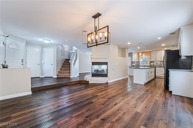 unfurnished living room featuring baseboards, recessed lighting, dark wood-style flooring, and a notable chandelier