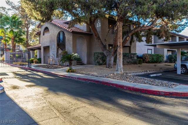 mediterranean / spanish house featuring a gate, a tiled roof, and stucco siding