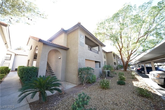 view of property exterior featuring central air condition unit, stairs, stucco siding, and a tile roof