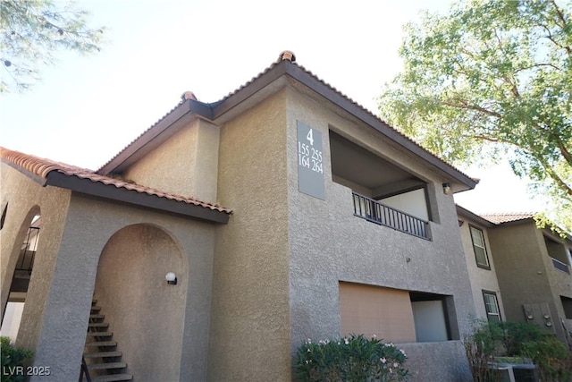 view of property exterior with a tiled roof, central AC unit, stucco siding, and a balcony