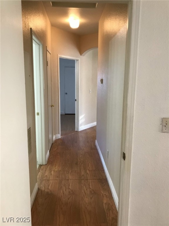hall featuring baseboards, arched walkways, and wood finished floors