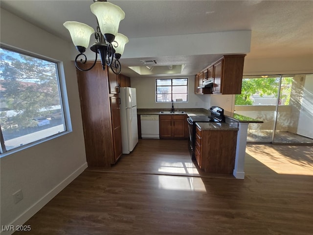 kitchen featuring dark countertops, white appliances, dark wood-type flooring, under cabinet range hood, and a notable chandelier