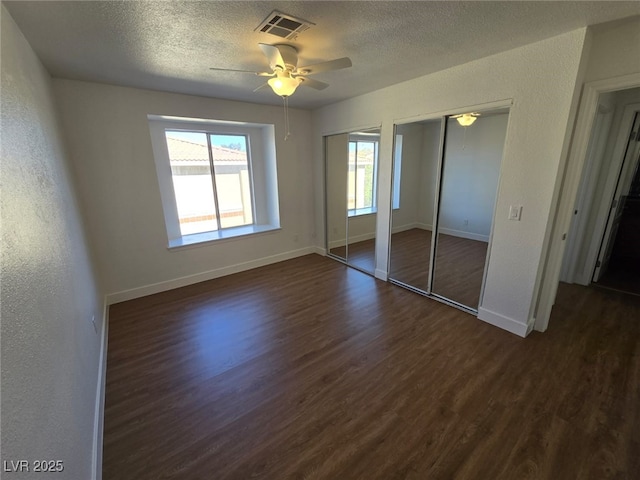 unfurnished bedroom featuring visible vents, multiple closets, dark wood-style flooring, baseboards, and a textured ceiling