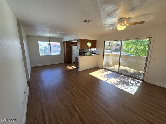 unfurnished living room featuring baseboards, a textured ceiling, ceiling fan with notable chandelier, and dark wood finished floors