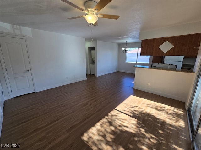 unfurnished living room with baseboards, ceiling fan with notable chandelier, and dark wood-type flooring