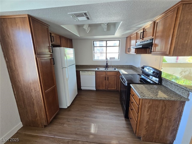 kitchen featuring visible vents, a sink, under cabinet range hood, white appliances, and dark wood-type flooring