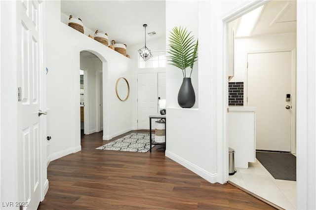 foyer featuring baseboards, arched walkways, wood finished floors, and visible vents