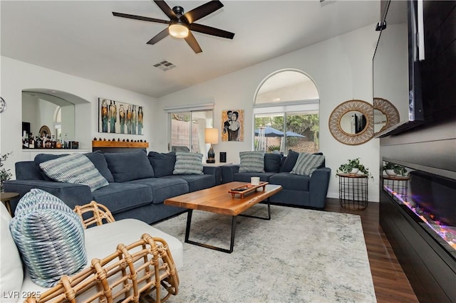 living room featuring dark wood-style flooring, ceiling fan, visible vents, and lofted ceiling
