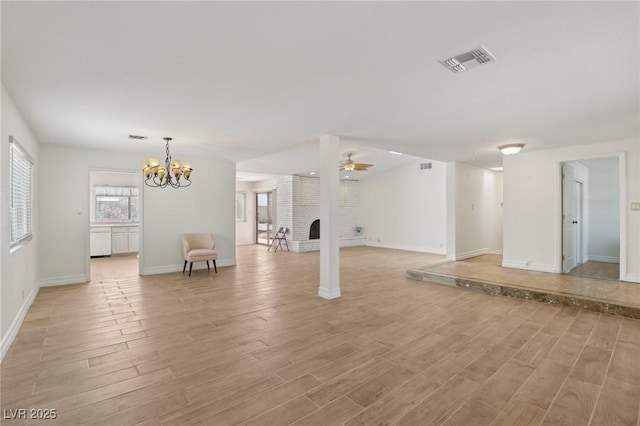 unfurnished living room with a fireplace, ceiling fan with notable chandelier, light wood-style flooring, and visible vents