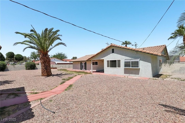 back of property with fence, stucco siding, and a tile roof